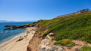 A coastal property with a beach, rocky terrain, and a house on a hill overlooking the sea.