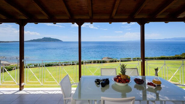 A covered outdoor dining area with a table set for two, overlooking a scenic ocean view.