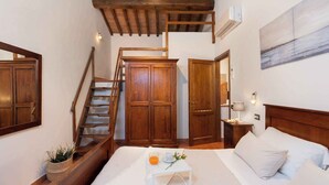A bedroom with a wooden staircase, a bed with white linens, a small table with a glass of orange juice, and a painting on the wall. - Villa with private pool and air conditioning (Villamagna)