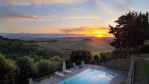 A pool with stone tiles and lounge chairs, surrounded by a stone wall and a view of rolling hills and a sunset. - Villa with private pool and air conditioning (Villamagna)