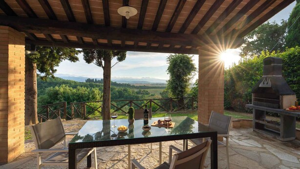 An outdoor patio with a glass table, chairs, and a brick barbecue grill. - Villa with private pool and air conditioning (Villamagna)