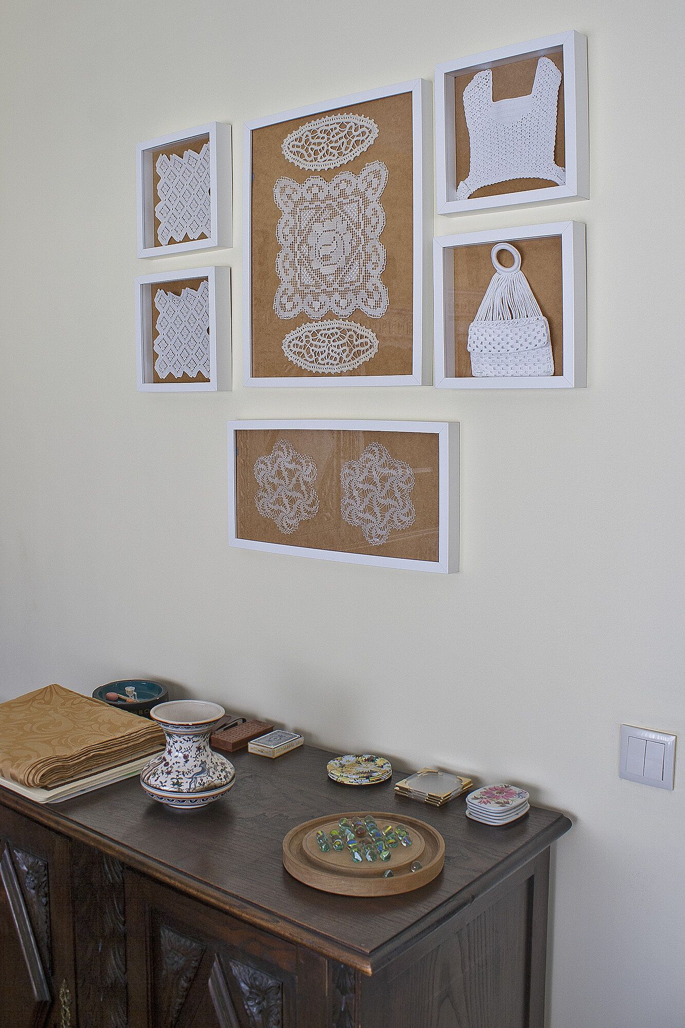 A wall with framed crochet artwork and a table with decorative items.