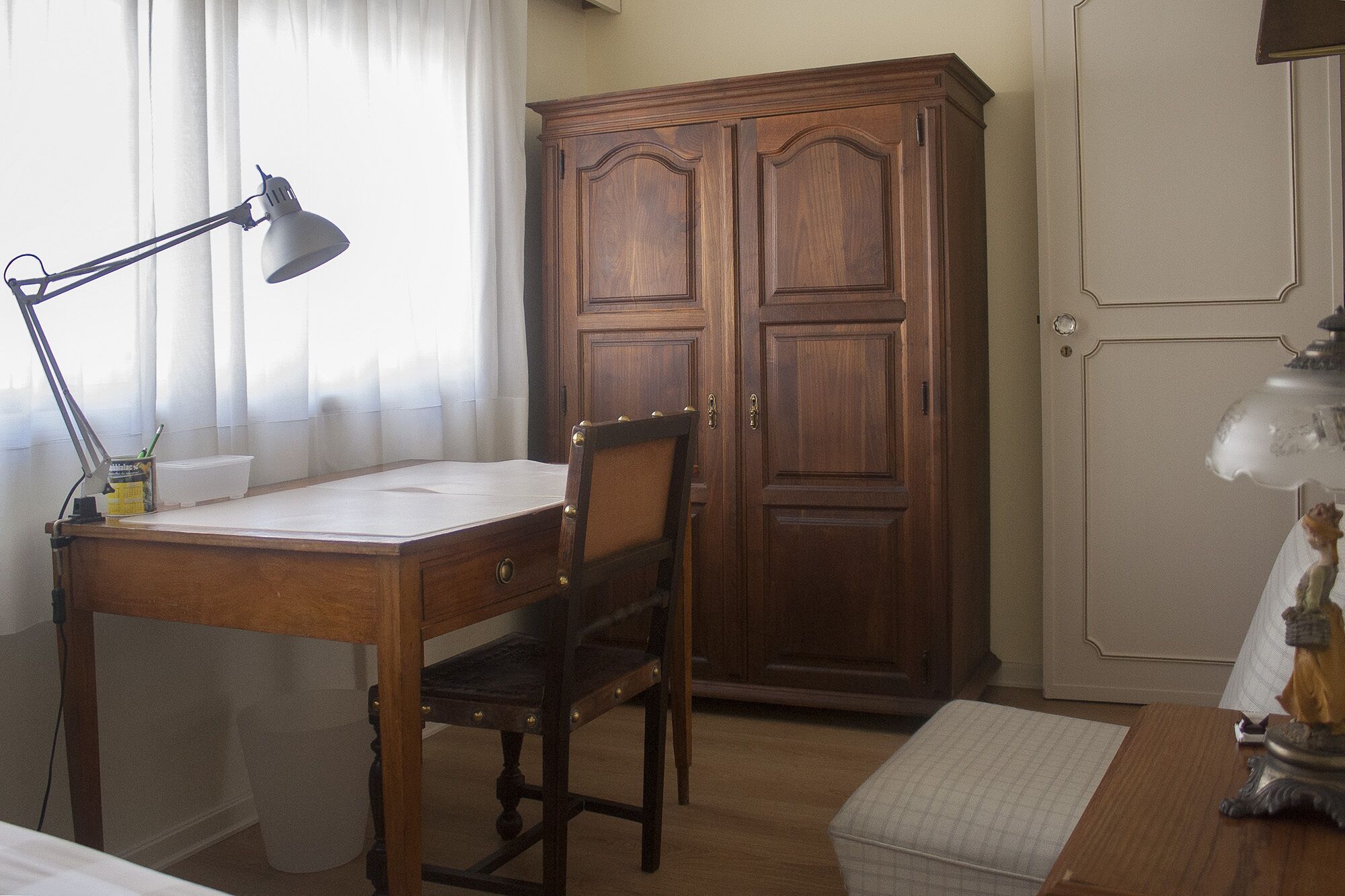 Ein Zimmer mit Holzschreibtisch, Stuhl, Lampe, Kleiderschrank und Bett.
