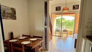 A dining area with a wooden table and chairs, a kitchen area with a refrigerator, and a balcony with chairs. - Cosy Studio w/ Mezzanine, Parking & Pools - 400m from Beach (Argelès-sur-Mer)