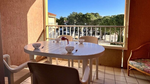 A balcony with a round table and chairs, a view of trees and a parking lot. - Cosy Studio w/ Mezzanine, Parking & Pools - 400m from Beach (Argelès-sur-Mer)