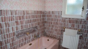 Une salle de bain avec une baignoire rose, une fenêtre à vitre dépolie et un mur à motifs.