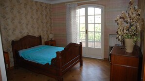 Une chambre à coucher avec un lit en bois, une table de chevet, une commode et une fenêtre avec des rideaux.