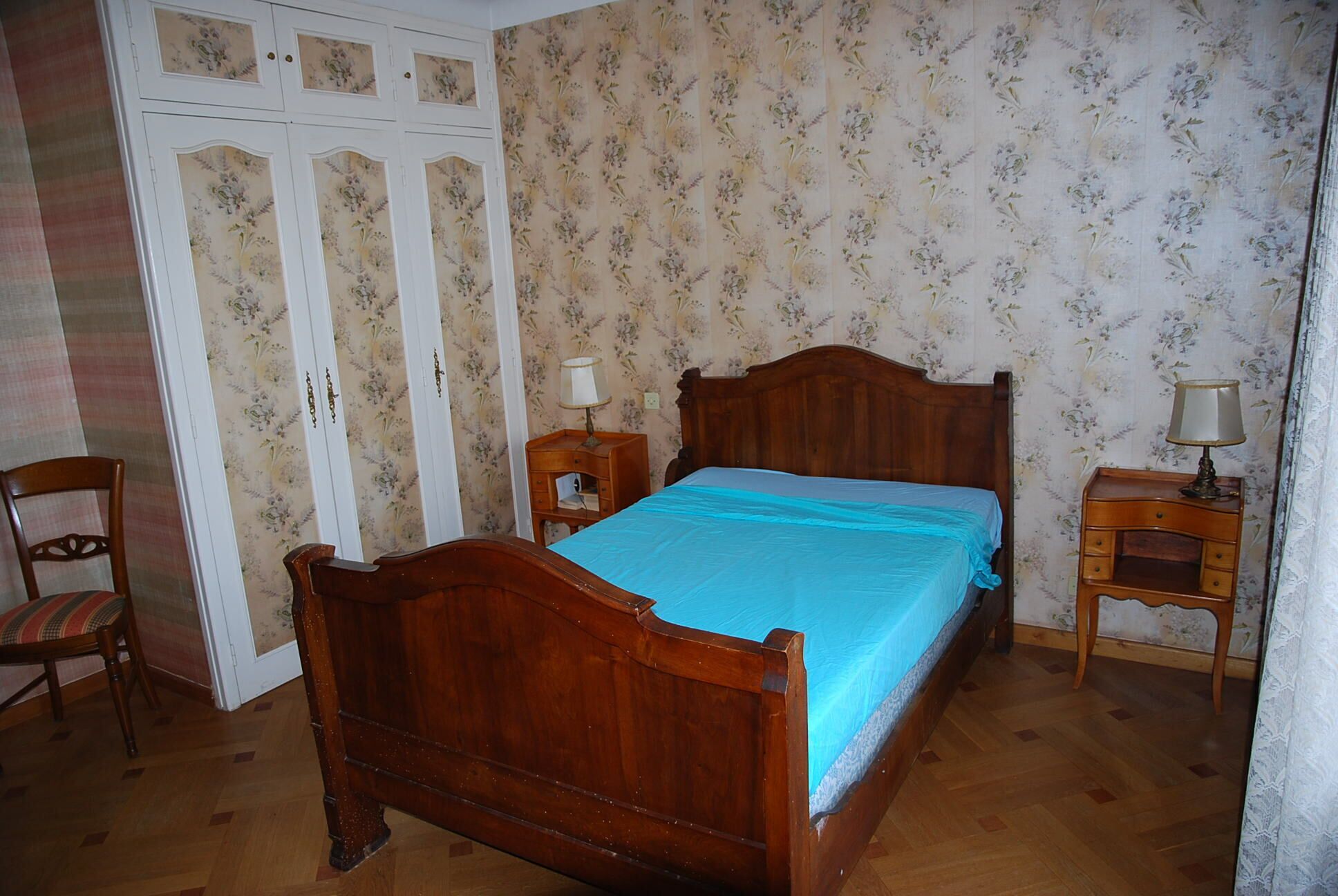 A bedroom with a wooden bed, a nightstand, a chair, and a wardrobe.