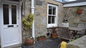 A stone building with a white door, potted plants, and outdoor seating. - St Ives Cottage near beach. Sleeps 4, with Courtyard Garden + Log Burner (Saint Ives)