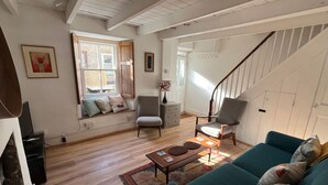 A spacious living room with a staircase, wooden floors, and a large window. - St Ives Cottage near beach. Sleeps 4, with Courtyard Garden + Log Burner (Saint Ives)