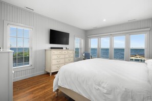 Un dormitorio con una cama grande, un aparador, un televisor y vistas al mar.