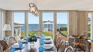 A dining area with a view of the sea, wooden walls, and a hanging light fixture. - The Ultimate Nantucket Sound Beachfront Oasis! (2144) (Dennis Port)