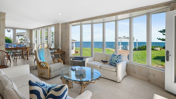A spacious living area with a glass coffee table, white sofas, and a view of the sea. - The Ultimate Nantucket Sound Beachfront Oasis! (2144) (Dennis Port)