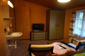 Cozy retreat with a single bed, table, and television, plus a convenient sink and wardrobe.