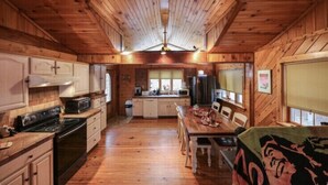 A wooden cabin interior with a kitchen, dining area, and a large window. - Stunning Lake Front Home (Glen Spey)