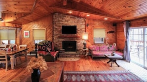 A log cabin interior with a stone fireplace, wooden ceiling, and a dining area with a table and chairs. - Stunning Lake Front Home (Glen Spey)