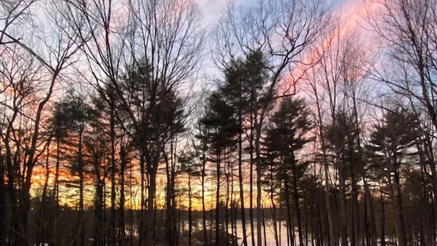 A hot tub on a wooden deck with a view of a forest and a sunset. - Stunning Lake Front Home (Glen Spey)