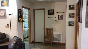 A living room with a leather couch, a wooden chair, and a radiator. There are framed pictures on the walls and a door leading to another room.