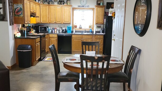 A kitchen with wooden cabinets, a dining table with chairs, a clock, and a welcome sign.
