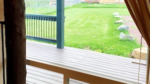 Een houten terras met een leuning, uitzicht op een gazon en een gebouw op de achtergrond.