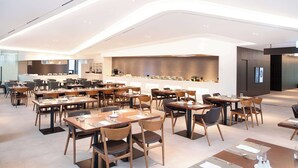 A modern dining area with multiple tables and chairs, a kitchen in the background, and a contemporary ceiling design. - Orakai Daehakro Hotel, BW Signature Collection (Seoul)