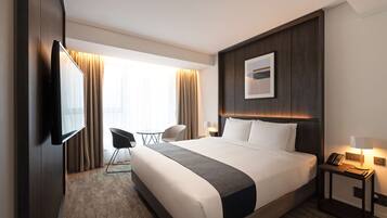 Una habitación de hotel moderna con una cama grande, un televisor de pantalla plana en la pared, un escritorio pequeño con una lámpara y una silla.