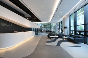 A modern reception area with a curved white reception desk, black sofas, and a large window offering a view of the outdoors. - Orakai Daehakro Hotel, BW Signature Collection (Seoul)