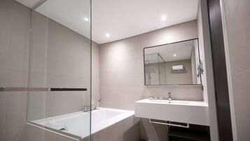 A modern bathroom with a glass-enclosed shower, a white bathtub, and a sink with a mirror above it.