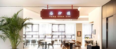 Un comedor moderno con una planta grande en maceta, mesas, sillas y un letrero que dice "Tang Chao Lou".