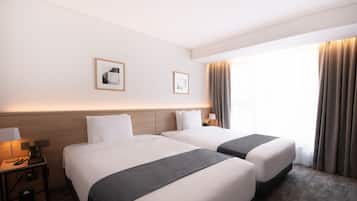 A hotel room with two beds, a nightstand with a lamp, and a window with curtains.