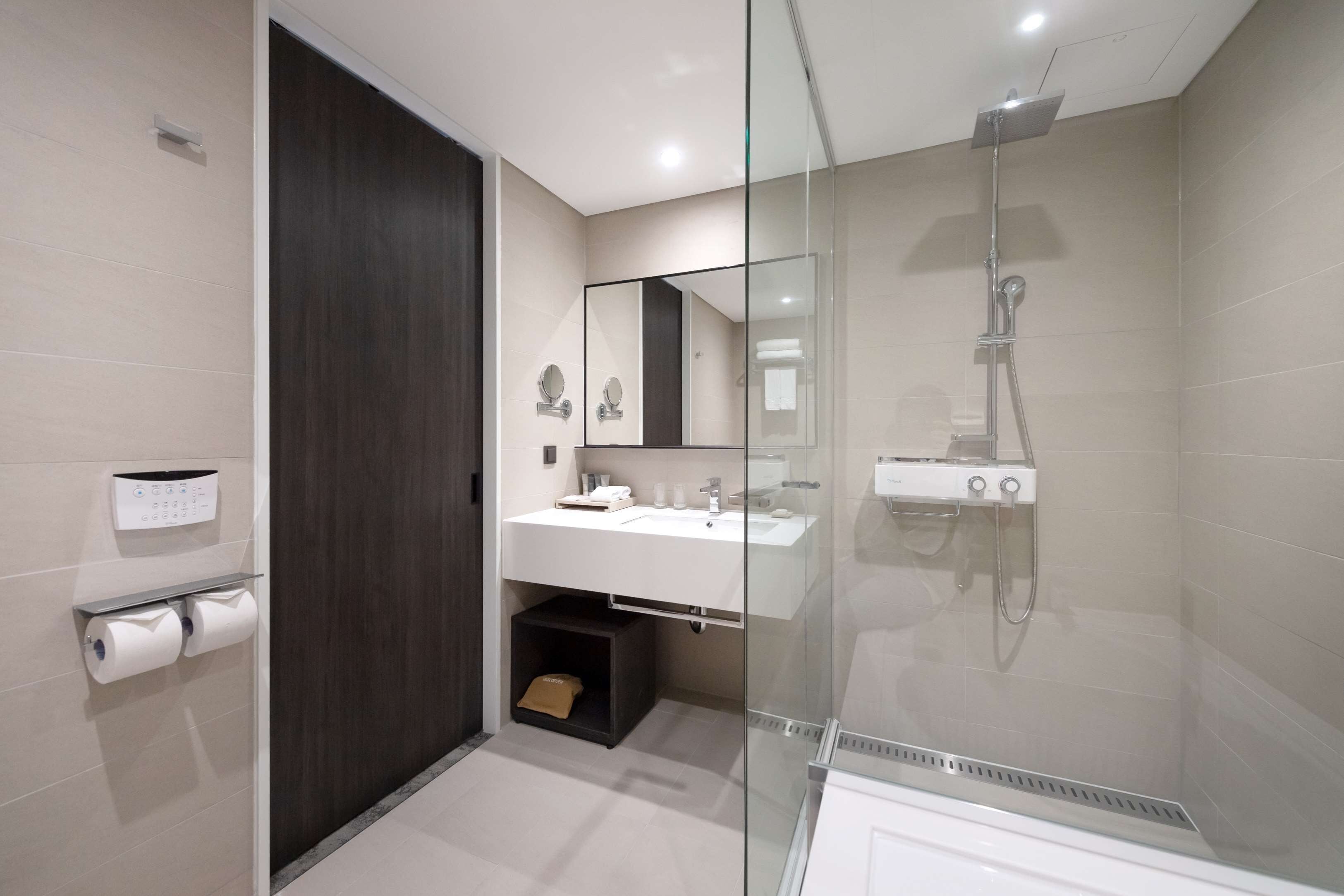 A modern bathroom with a glass shower enclosure, a dark wooden door, and a white sink with a mirror above it.