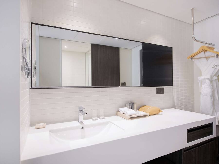 A modern bathroom with a large mirror, white tiles, a sink, and a towel rack.