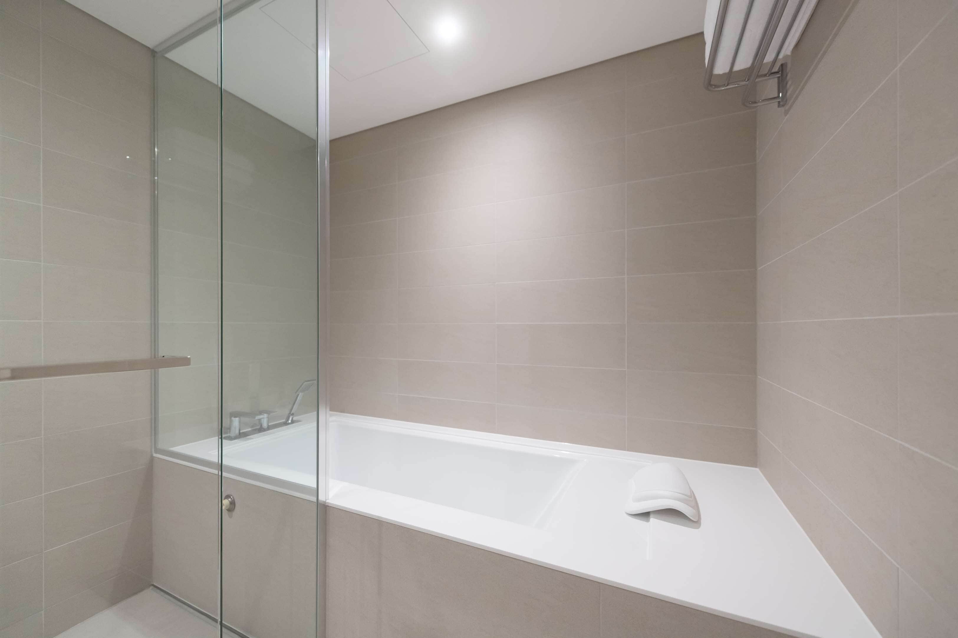 A modern bathroom with a glass-enclosed shower, a white bathtub, and beige tiles.