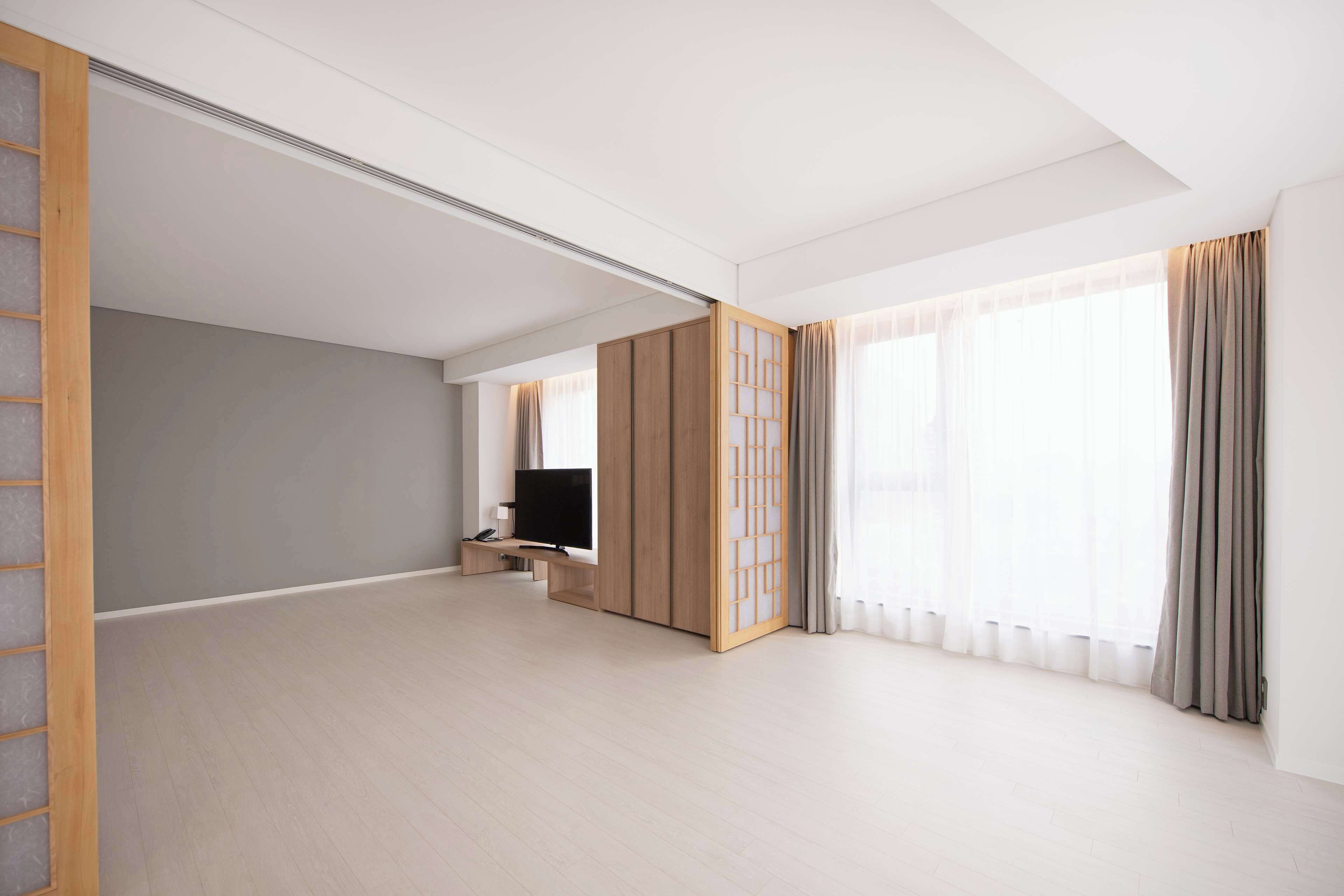 Una habitación amplia con un ventanal grande, televisor y puerta corredera.