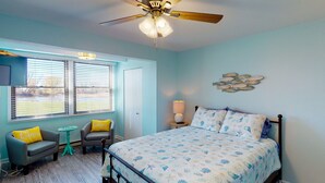 A bedroom with a bed, a chair, a small table, a ceiling fan, and a window with blinds. - Jo's Hideaway, for Lake Erie lovers, fishermen and birders!  Sleeps 4 (Oak Harbor)