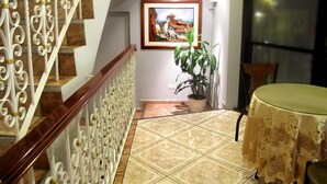 A staircase with ornate white railings, a potted plant, a framed picture on the wall, and a round table with a tablecloth. - Hotel Solís Dies (Lima)