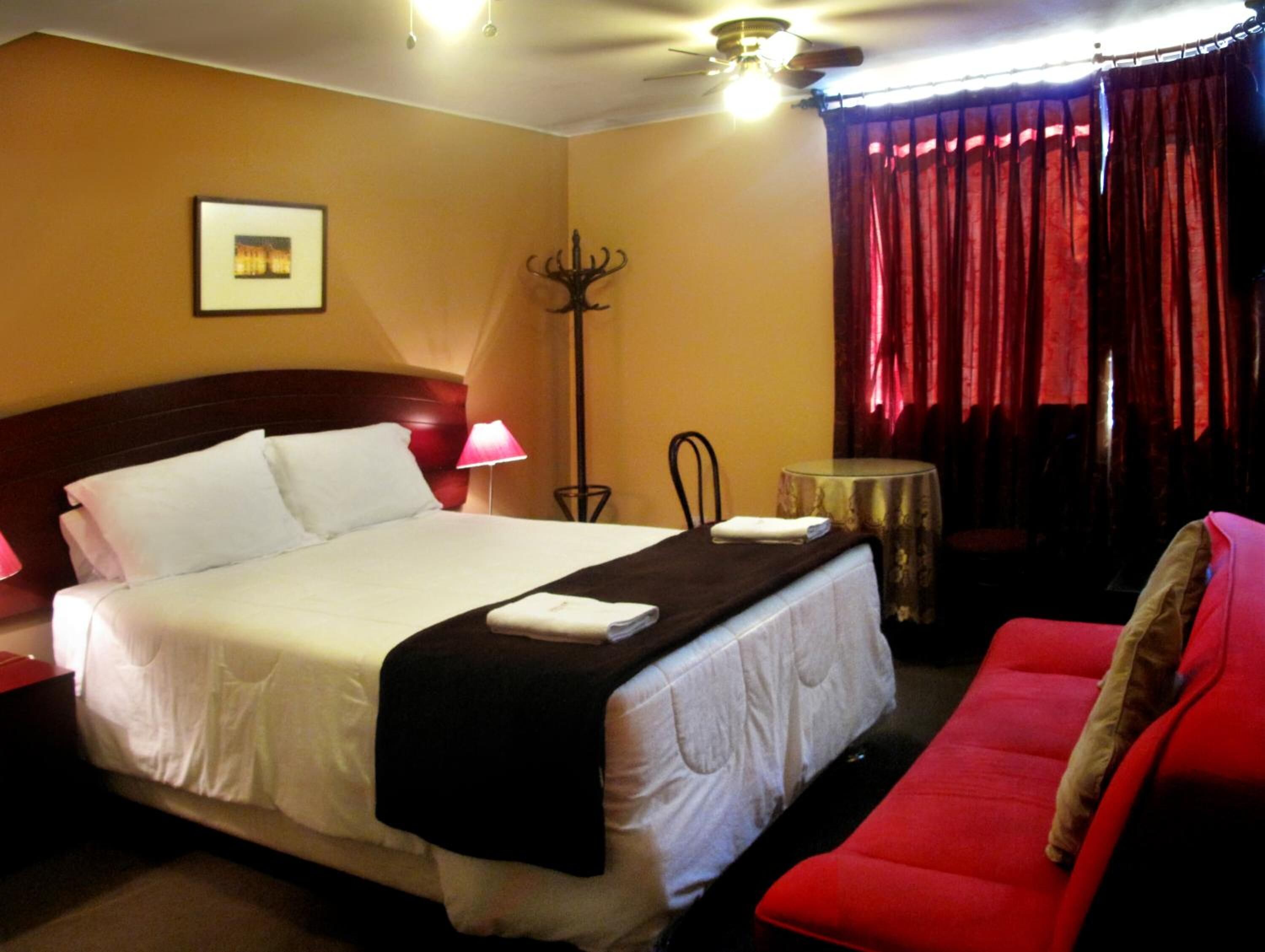 A hotel room with a bed, a red sofa, a lamp, a small table, and a picture on the wall.