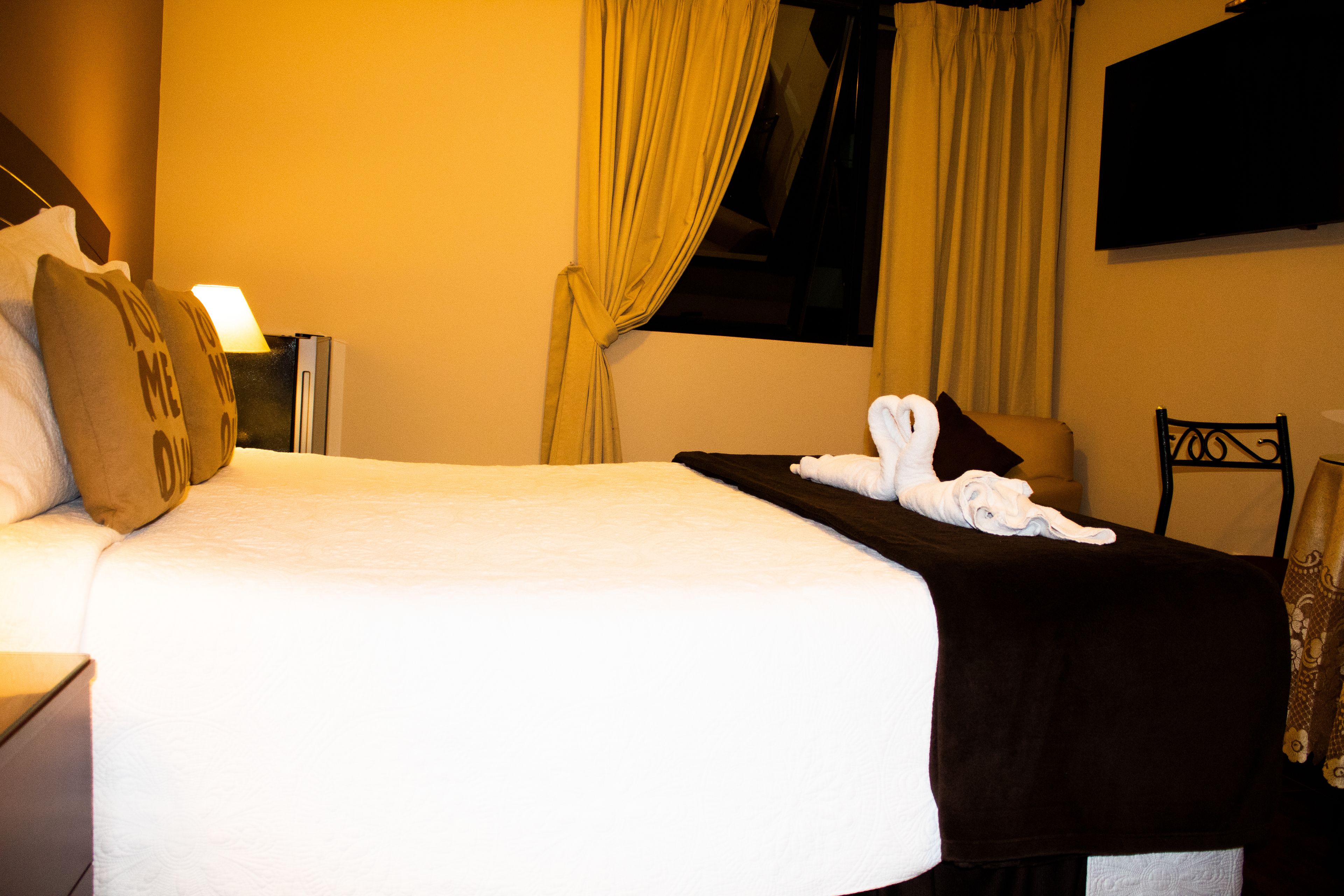 A hotel room with a bed, a nightstand, a lamp, and a TV mounted on the wall.
