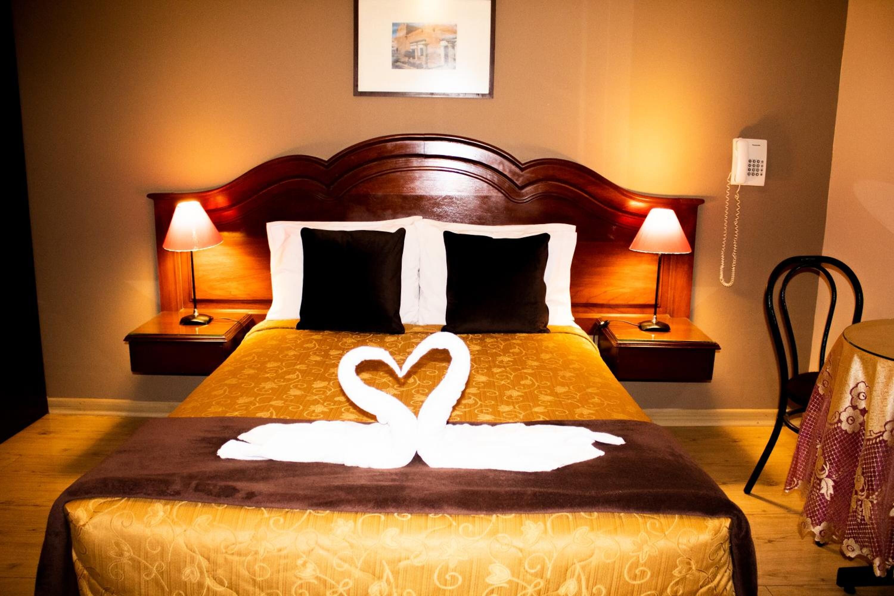 Ein Hotelzimmer mit einem Bett, zwei Nachttischlampen, einem Telefon und einem kleinen Tisch mit Tischdecke.