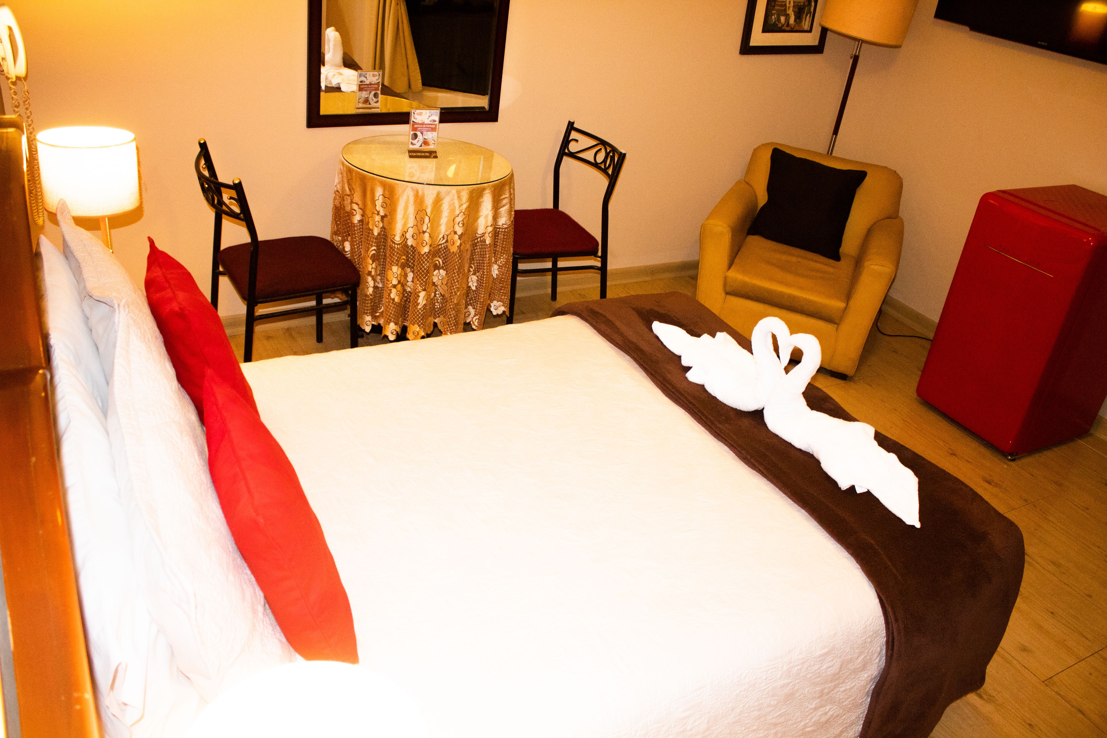 Hotelkamer met een bed, twee stoelen, een tafel, een lamp, een televisie en een rode kast.