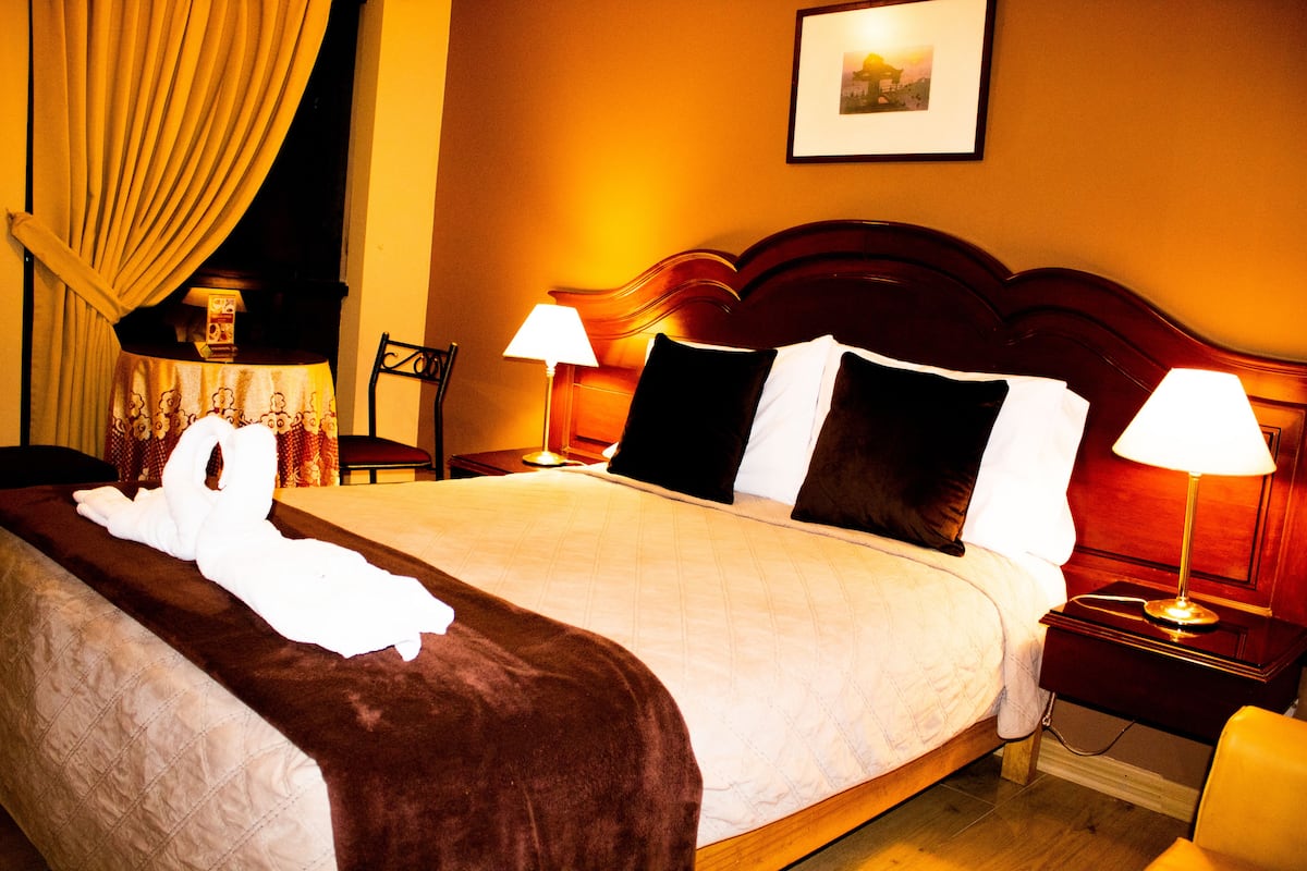 A hotel room with a large bed, two bedside lamps, a framed picture on the wall, and a chair.