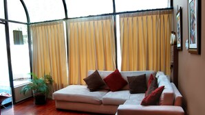A modern living room with a sectional sofa, a potted plant, and a large window with curtains. - Hotel Solís Dies (Lima)