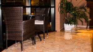 A lobby with a seating area featuring wicker chairs and a table, a large potted plant, and a tiled floor. - Hotel Solís Dies (Lima)