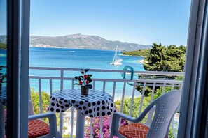 Ein Balkon mit Blick auf das Meer, ein Segelboot und ferne Berge.