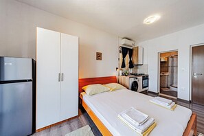 A bedroom with a bed, a wardrobe, a kitchenette, and a bathroom.