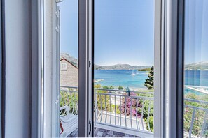 A balcony with a view of the sea, a sailboat, and distant mountains.