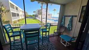 Uma varanda com mesa e cadeiras, vista para uma piscina e um edifício ao fundo.