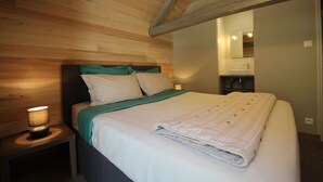 Ein ordentlich bezogenes Bett mit grüner Decke und weißen Kissen, einer Nachttischlampe und einer Holzbalkendecke.
