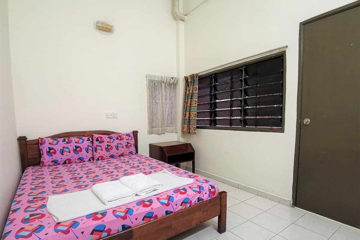A bedroom with a bed, a small wooden nightstand, a window with curtains, and a door.