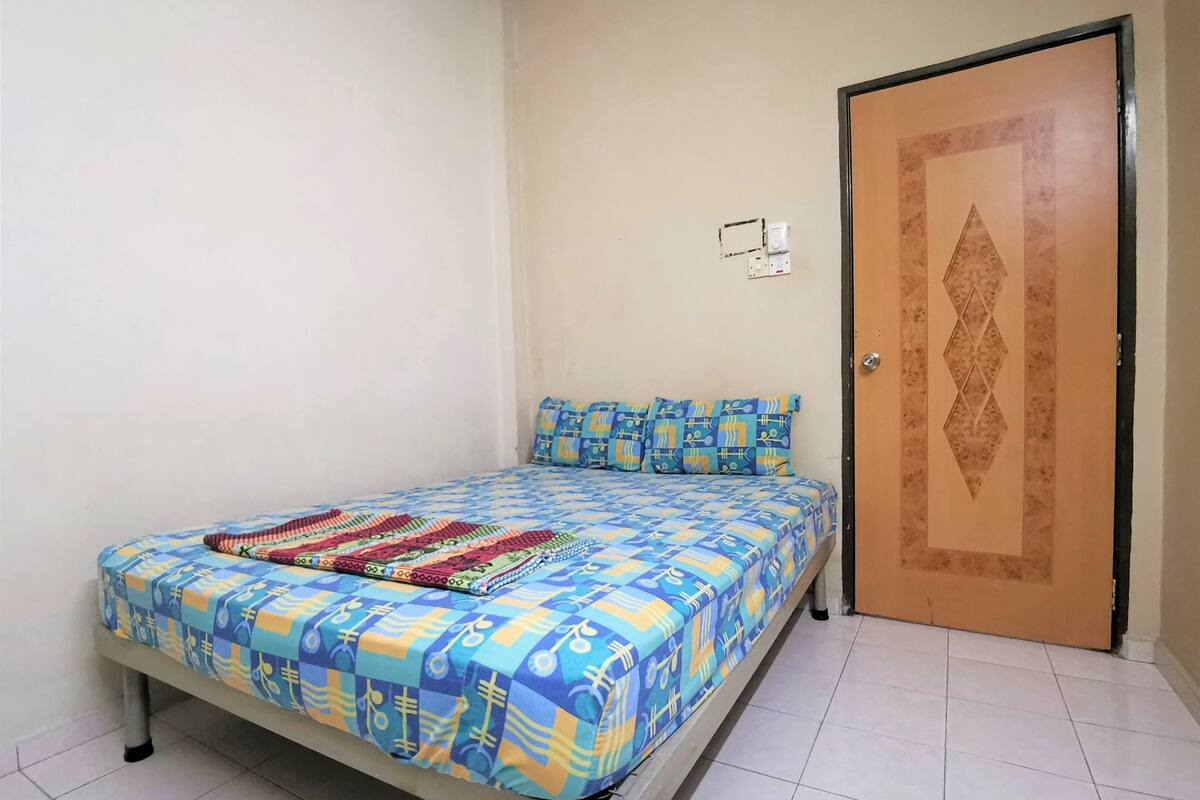 A single-bed room with a patterned bedspread, a door with a geometric design, and a light switch on the wall.